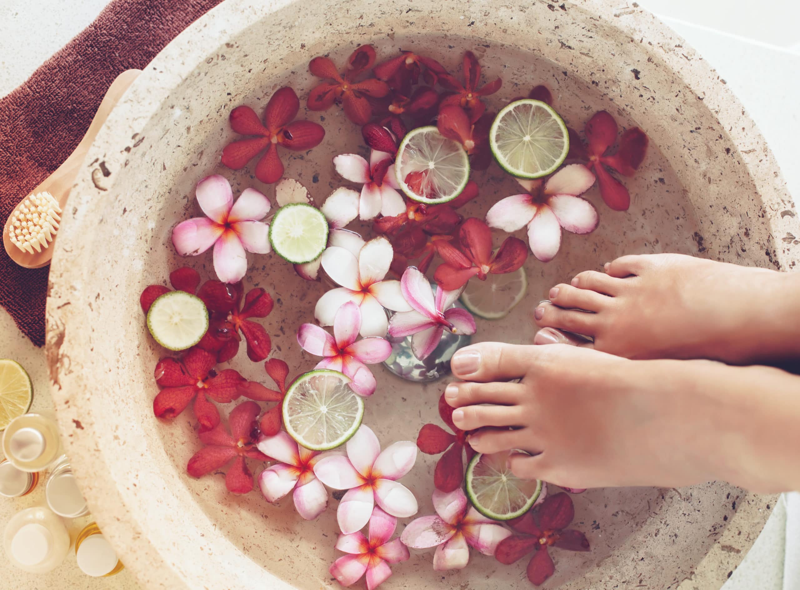 Foot bath in bowl with lime and tropical flowers, spa pedicure treatment, top view